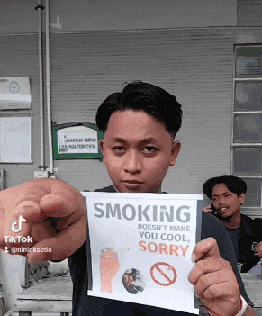 a young man is holding a sign that says smoking does n't make you cool sorry