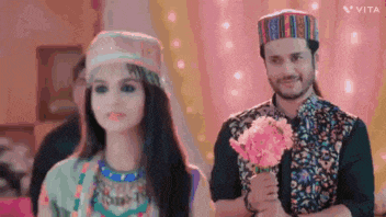 a man and a woman are standing next to each other holding a bouquet of pink flowers .