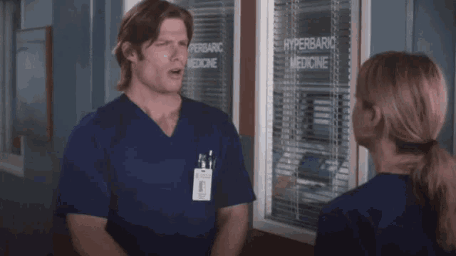 a man and a woman are standing in front of a window that says " hyperbaric medicine "