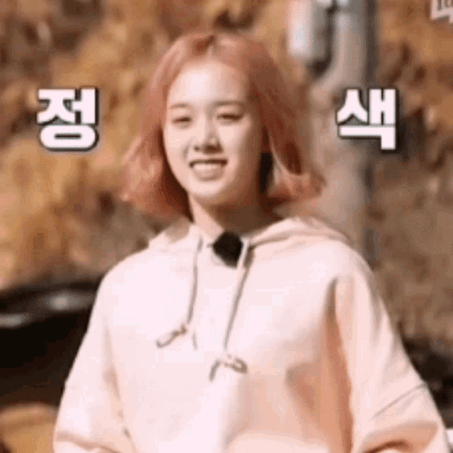 a girl with pink hair is wearing a pink hoodie and smiling in a foreign language .