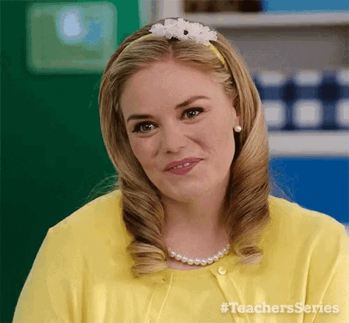 a woman in a yellow shirt and pearl necklace is smiling and looking at the camera .