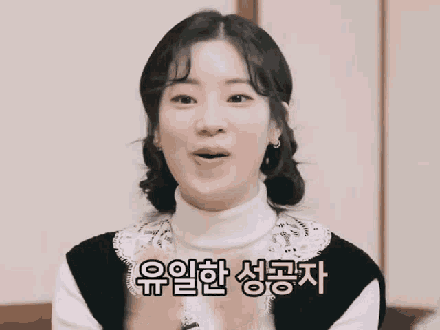 a woman wearing a white turtleneck and a black vest is smiling in a foreign language