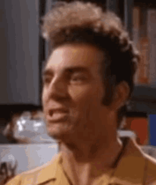 a close up of a man in a yellow shirt making a funny face in a kitchen .