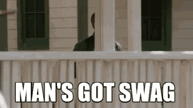 a man is standing on a porch with the words `` man 's got swag '' written on the screen .