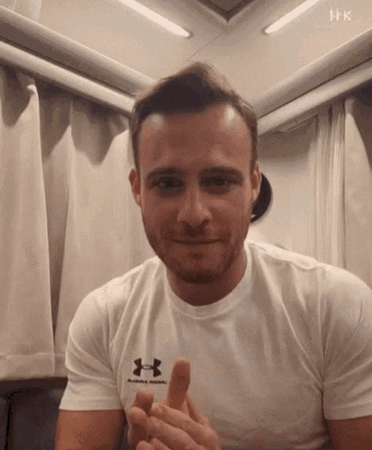 a man wearing a white under armour t-shirt giving a thumbs up