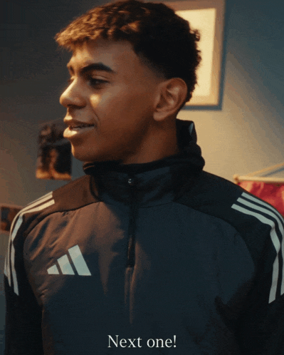 a man in a black adidas jacket is next to a sign that says next one