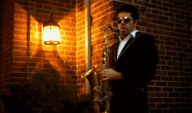 a man wearing sunglasses is playing a saxophone in front of a brick wall