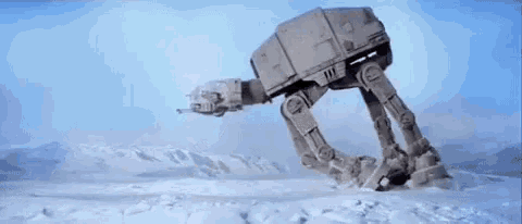 an at at robot is walking through the snow in a snowy field .