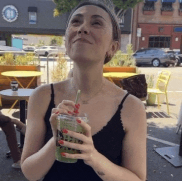 a woman in a black tank top drinking a green smoothie with a straw
