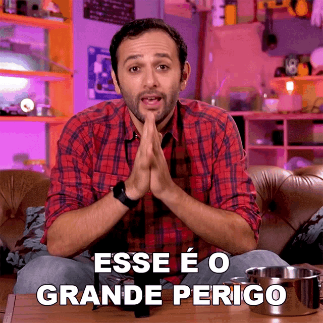 a man in a plaid shirt is sitting on a couch with the words " esse e o grande perigo " written above him