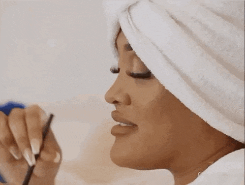 a woman with a towel wrapped around her head is applying makeup to her face .