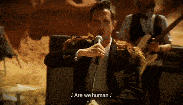 a man singing into a microphone with the words " are we human " next to him