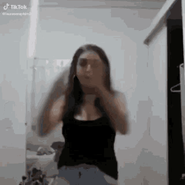 a woman in a black tank top is dancing in front of a mirror in a room .
