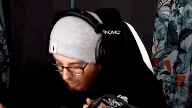 a man wearing glasses and a beanie is sitting in a chair with headphones on .
