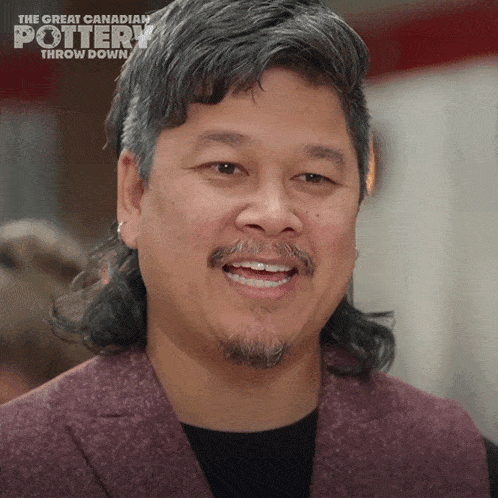 a man with long hair and a beard is smiling in front of a sign that says " the great canadian pottery throw down "