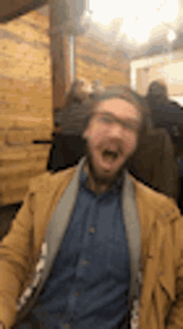 a man with a beard and glasses is making a funny face while sitting in a chair .