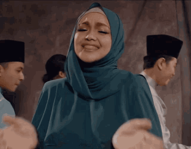 a woman wearing a hijab is smiling with her hands outstretched in front of a group of men