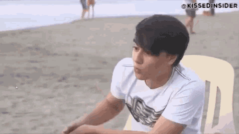 a young man is sitting on a chair on the beach .
