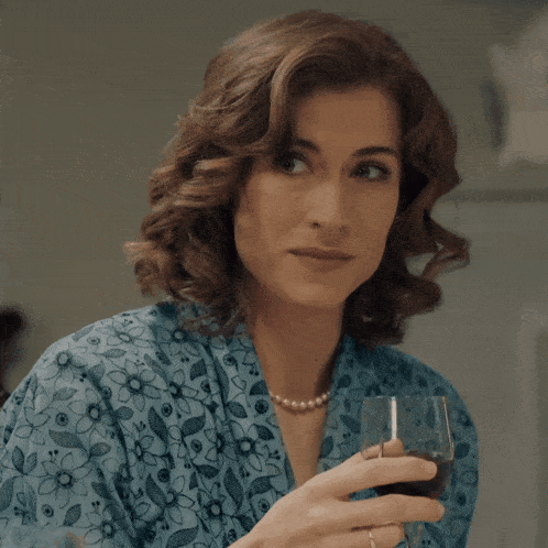 a woman wearing a blue floral shirt is holding a glass of wine
