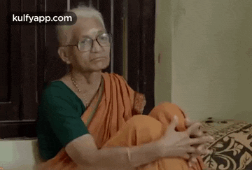 an elderly woman is sitting on a couch wearing glasses and a green shirt .