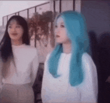 two girls with blue hair are standing next to each other and looking at something .