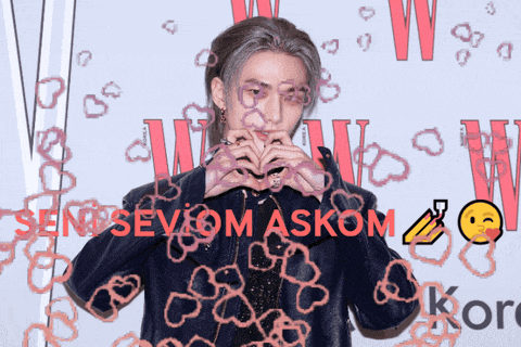 a man making a heart with his hands in front of a sign that says sen sev om askom