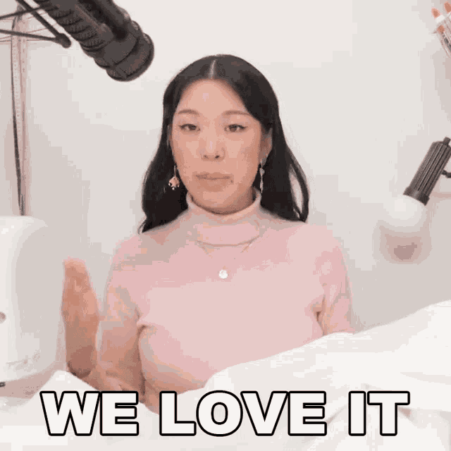 a woman in a pink sweater says we love it in front of a microphone