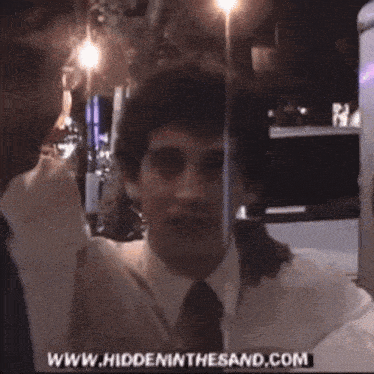 a man in a white shirt and tie is smiling in front of a sign that says www.hiddeninthesand.com