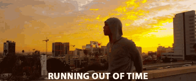 a man in a hoodie is running out of time in front of a sunset