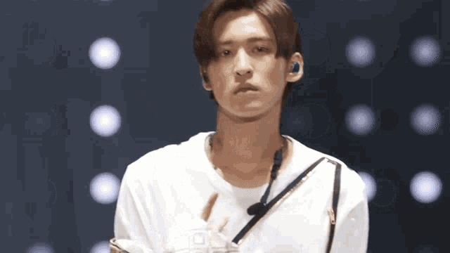 a young man wearing a white t-shirt and headphones stands on a stage