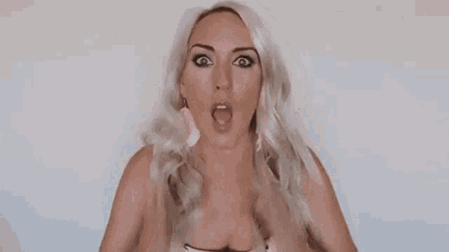 a woman with blonde hair is making a surprised face while holding her face with her hands .