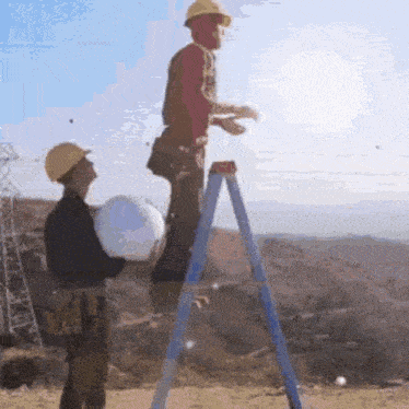 a man in a hard hat is standing on a ladder while another man stands behind him holding a bucket .