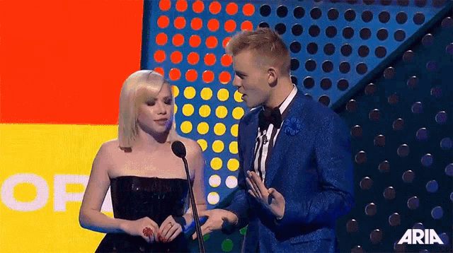 a man and a woman are standing next to each other on a stage at a awards show .