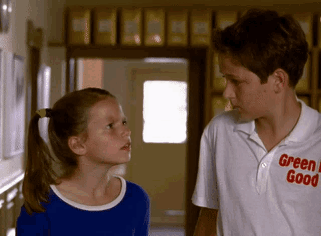 a boy and a girl are standing in a hallway and the boy is wearing a green good shirt