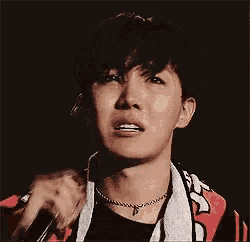 a man is crying while holding a microphone and wearing a scarf around his neck .