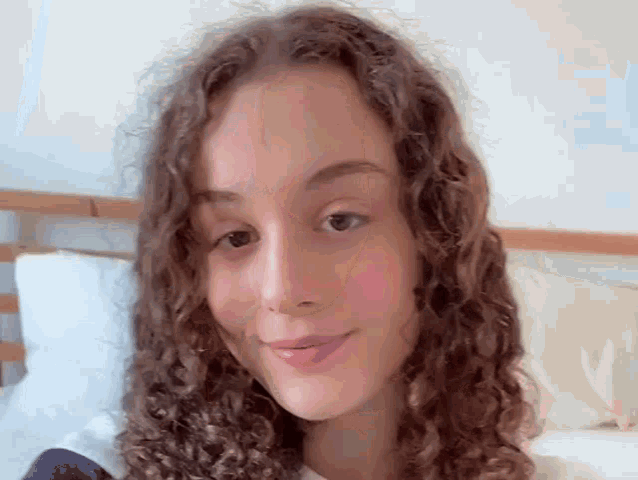 a young woman with curly hair is sitting on a bed smiling .