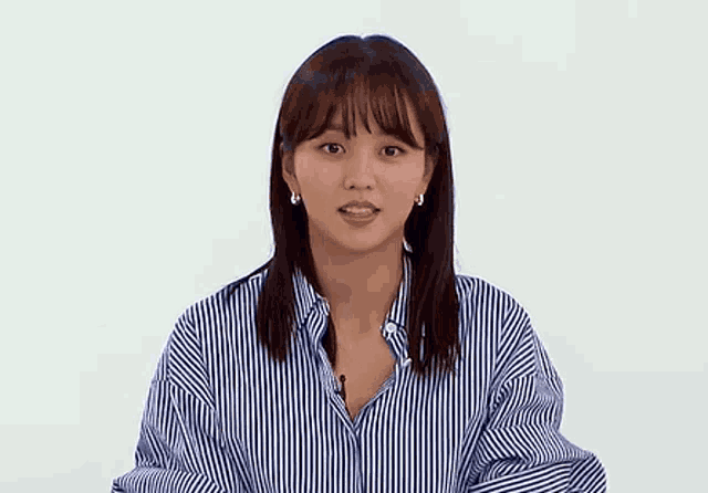 a woman wearing a blue and white striped shirt and earrings is making a face .