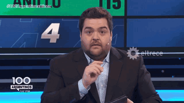 a man in a suit stands in front of a screen that says 100 argentinas dicen