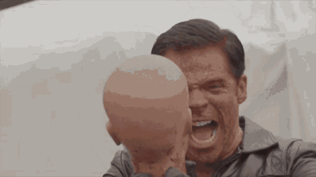 a man with blood on his face is holding a bald head with his mouth open .