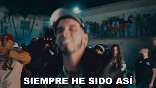 a man in a baseball cap stands in front of a crowd and says " siempre he sido así "
