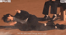 a man is laying on the ground while another man sits on a stool behind him