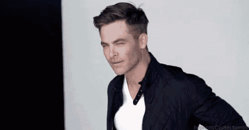 a man wearing a black jacket and a white t-shirt is winking at the camera .