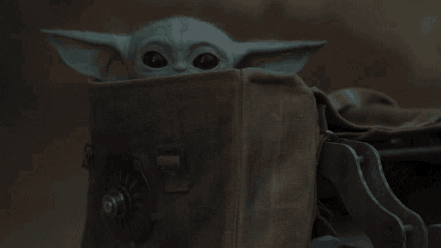 a baby yoda is sitting in a brown bag and looking at the camera