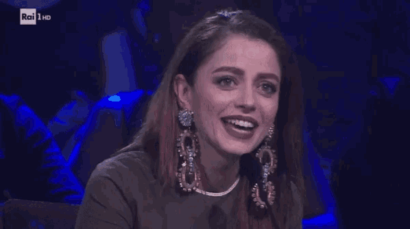 a woman wearing earrings is smiling and clapping her hands in front of a microphone ..