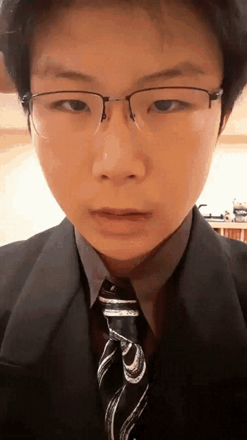 a young man wearing glasses and a black suit