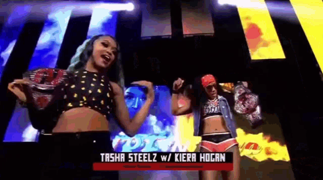 two women are dancing in front of a large screen that says tasha steelz w / kiera hogan .