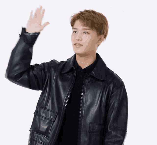 a young man wearing a black leather jacket is waving his hand