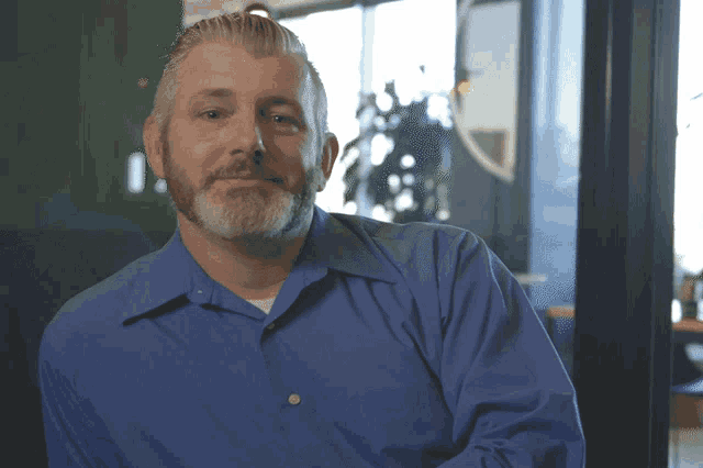 a man with a beard wearing a blue shirt looks at the camera