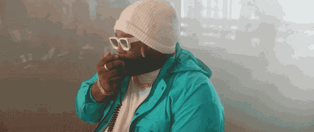 a man wearing a beanie and sunglasses holds his hand over his mouth