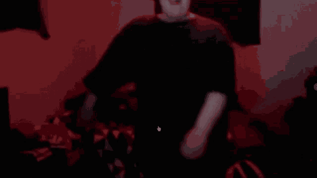 a man in a black shirt is dancing in a dark room with red lights .